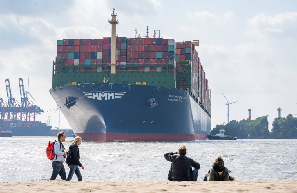 Das größte Containerschiff der Welt im Hamburger Hafen: Der Frachter Algeciras der Hyundai Merchant Marine legt am Containerterminal Burchardkai der HHLA in Hamburg Waltershof an – Passanten beobachten die Ankunft und das Anlegemanöver vom Elbstrand aus. Foto: imago images / Chris Emil Janßen