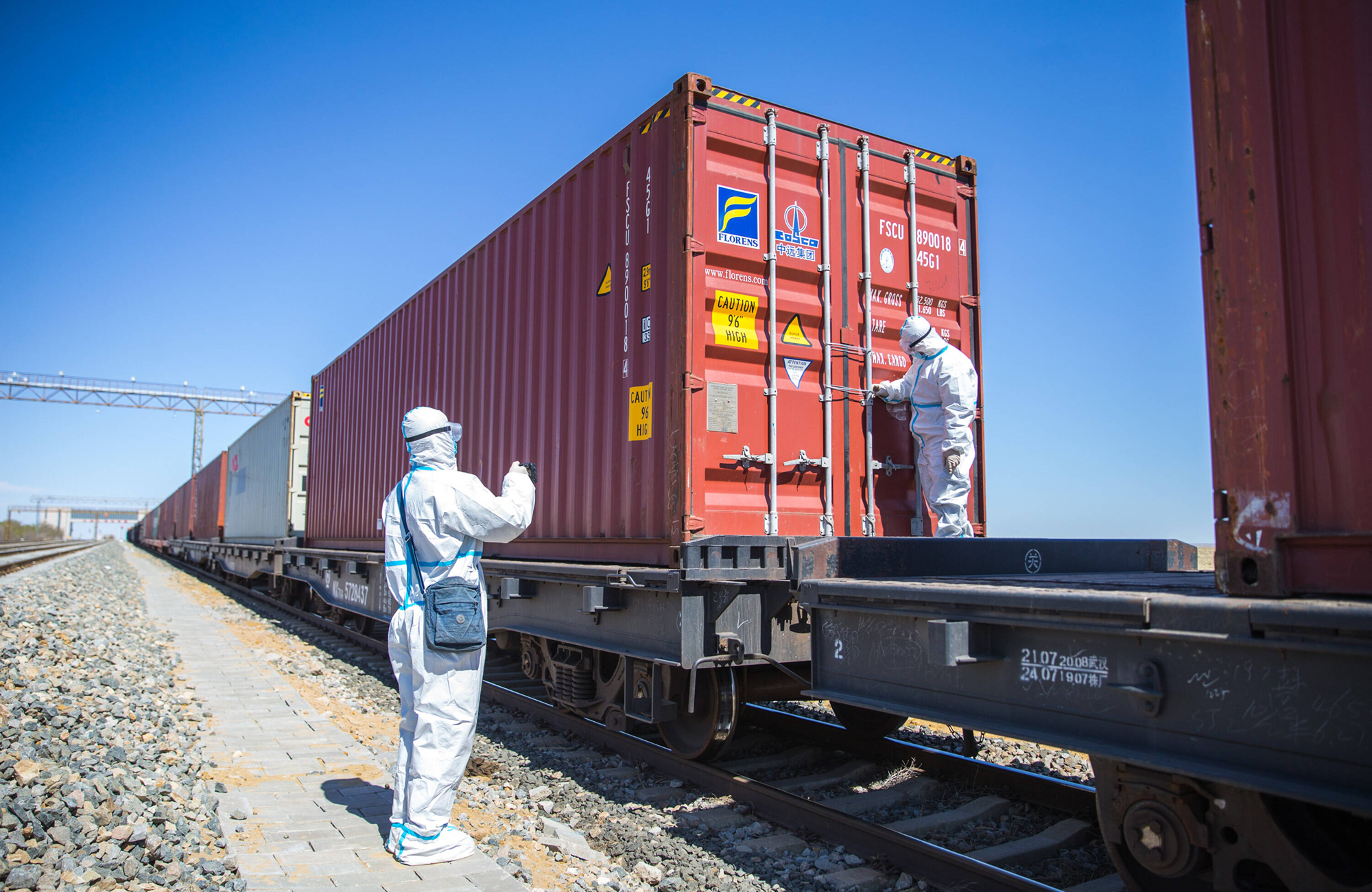 Nachfragerückgänge im Ausland, Störungen in internationalen Lieferketten, Transportschwierigkeiten und Grenzkontrollen haben in der Coronakrise zu einem drastischen Einbruch des deutschen Außenhandels geführt. Hier kontrollieren Polizeibeamte in Schutzausrüstung am Grenzübergang in Erenhot (Innere Mongolei) einen Güterzug, der als China-Europe Railway Express unterwegs ist (Aufnahme vom 29. April 2021). Foto: IMAGO / VCG